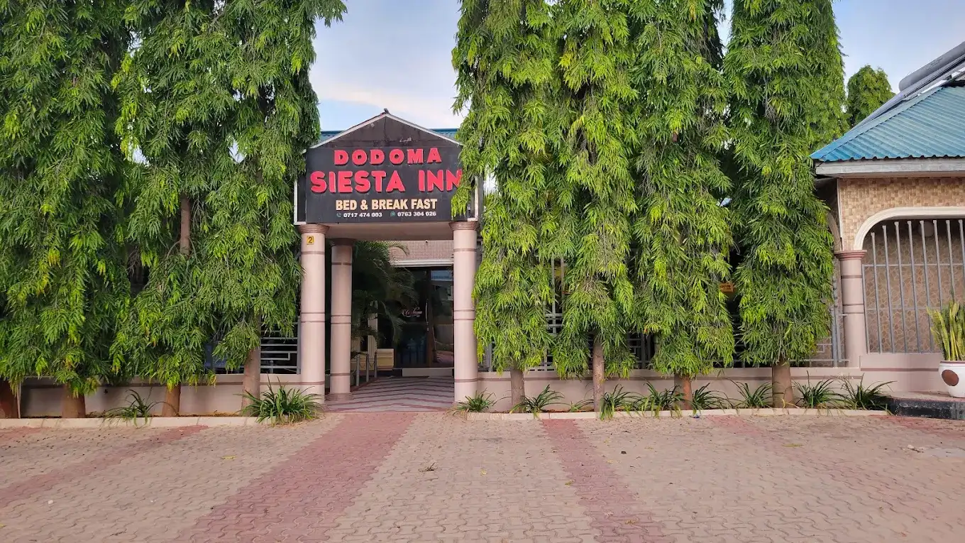The entrance arch of Dodoma Siesta Inn between two tall trees on a clear day